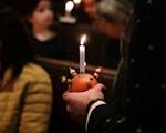 Photograph of a person holding a Christingle candle - an orange with four cocktail sticks attached to the fruit with threaded sweets and raisons and a lit candle in the centre