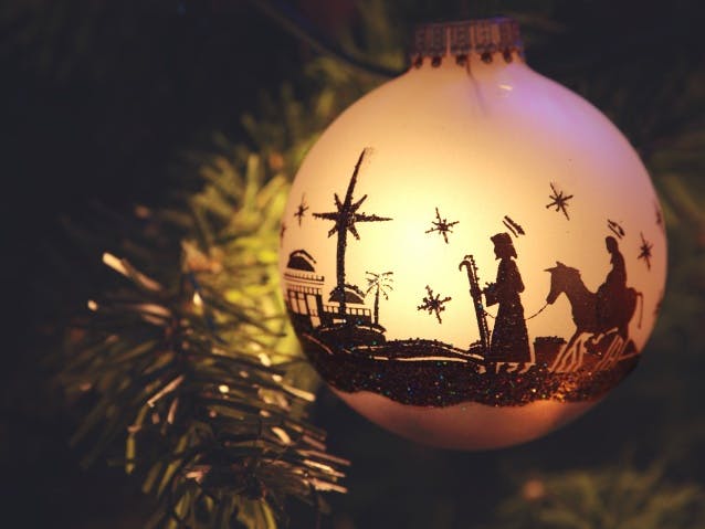 Image courtesy of cstar55 from Getty Images Signature via canva.com Photograph of a bauble with the nativity image of Joseph and Mary on a donkey with stars in the sky etched on the side,. It is lit up on a Christmas tree