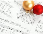 Photo of sheet music for christmas carols including Silent Night, with two baubles on the top right of image, one red and one gold
