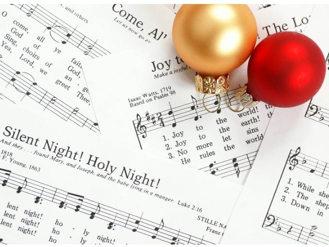 Photo of sheet music for christmas carols including Silent Night, with two baubles on the top right of image, one red and one gold