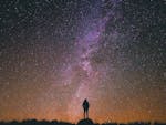 silhouette of a person standing on a rock while looking into the night's sky