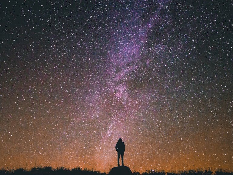 Stargazing courtesy of Greg Rakozy on Unsplash silhouette of a person standing on a rock while looking into the night's sky
