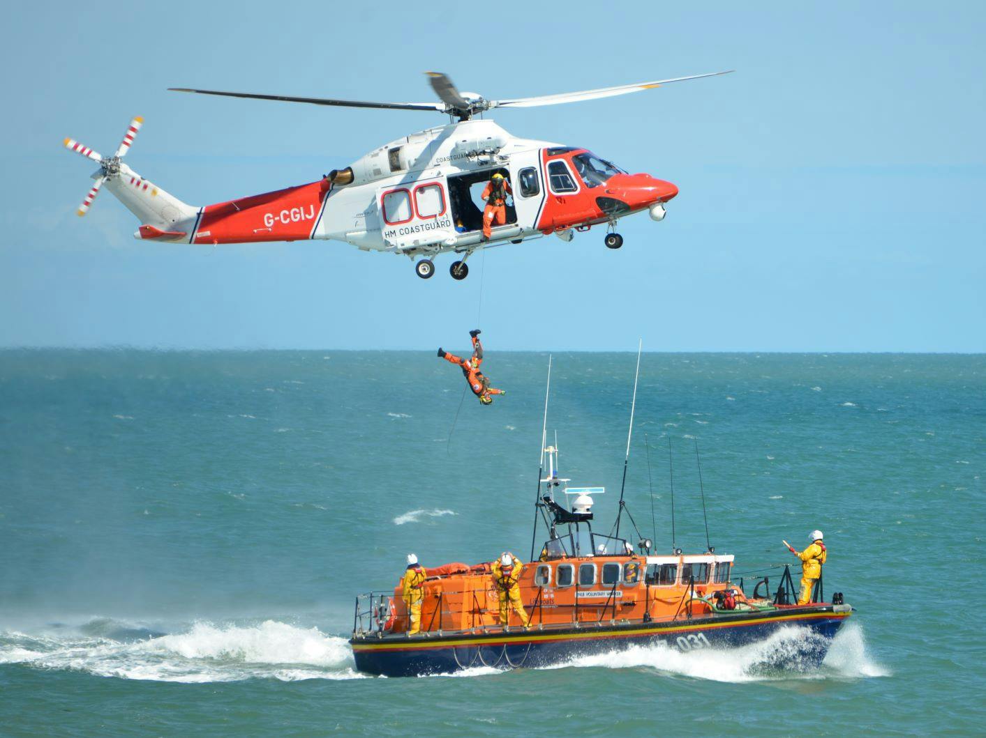Photograph of a coastguard helicopter carrying out a rescue maneuver over a RNLI Lifeboat
