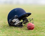Photograph of a blue cricket helmet and red cricket ball on grass