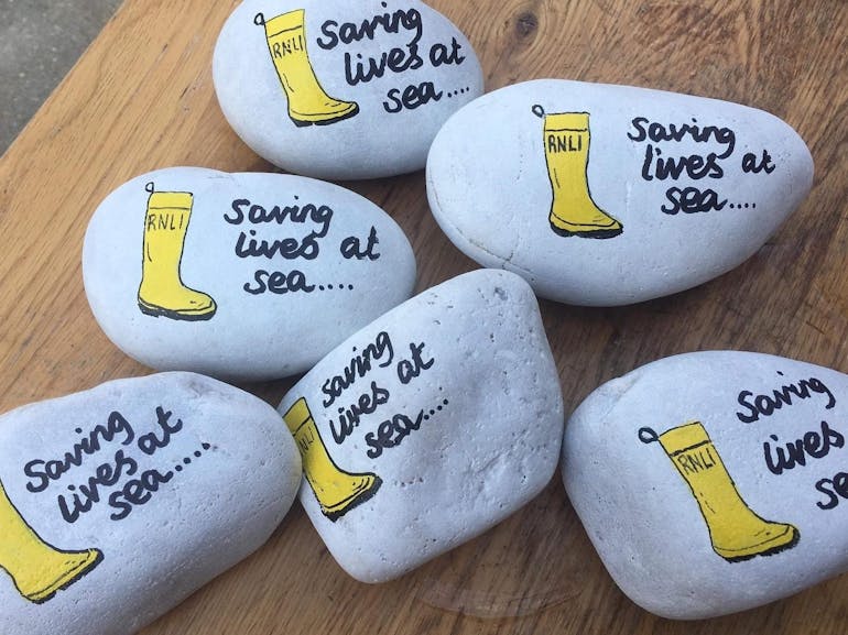 Pebbles for the Treasure Hunt courtesy of RNLI Selsey Photograph of a collection of pebbles painted with RNLI yellow boots and the words saving lives at sea