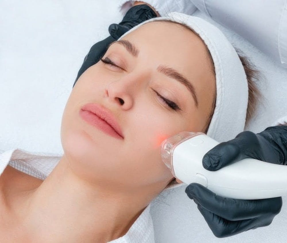 A woman undergoing a facial treatment with a device on her cheek, as part of a professional skin care procedure.