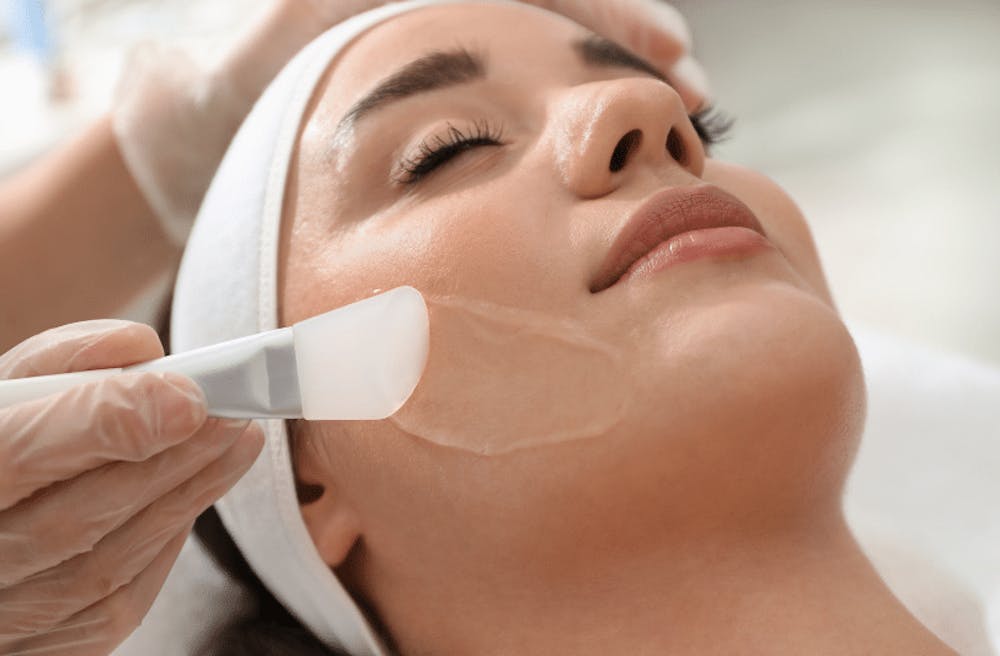 A woman lying on a spa bed receiving a gentle skin care treatment with a facial mask being applied to her face.