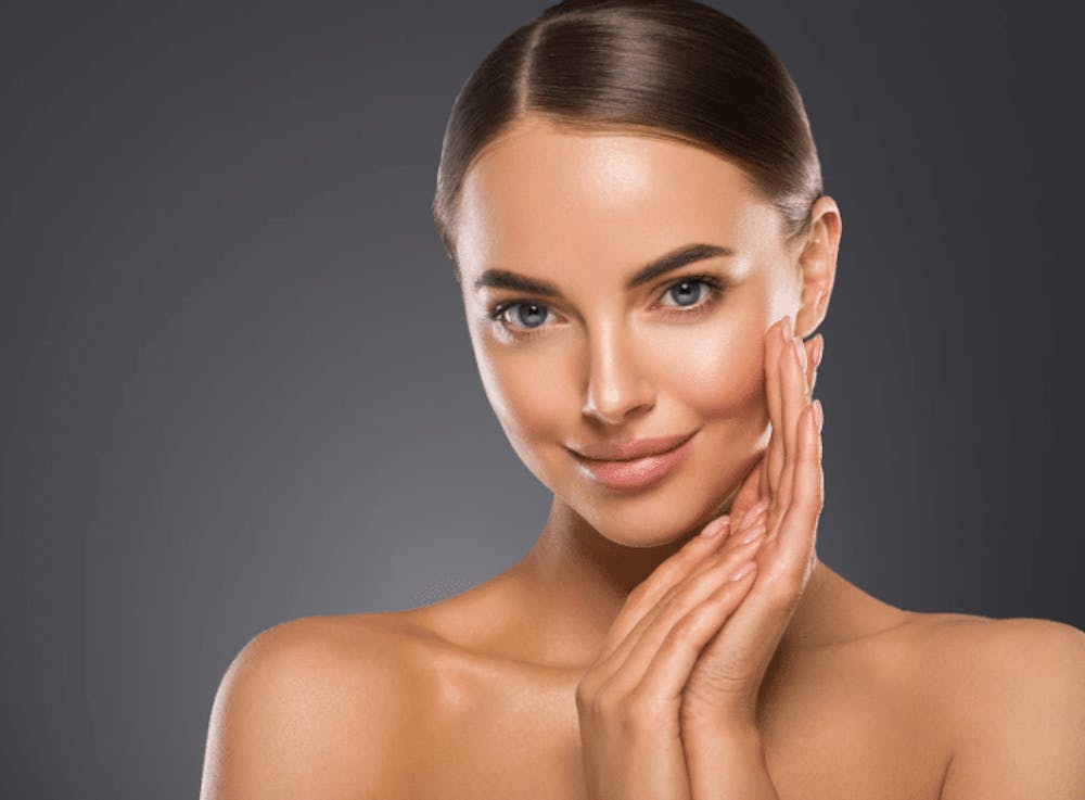 A woman with glowing skin, gently touching her face and smiling, showing the results of a consistent skin care routine.