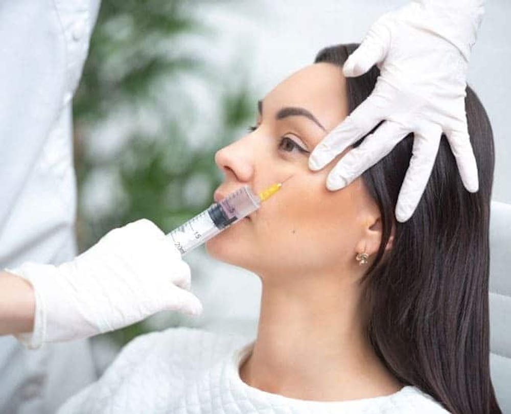 A close-up of a woman receiving a hyaluronic acid injection in a cosmetic treatment, with a focus on the syringe and procedure.