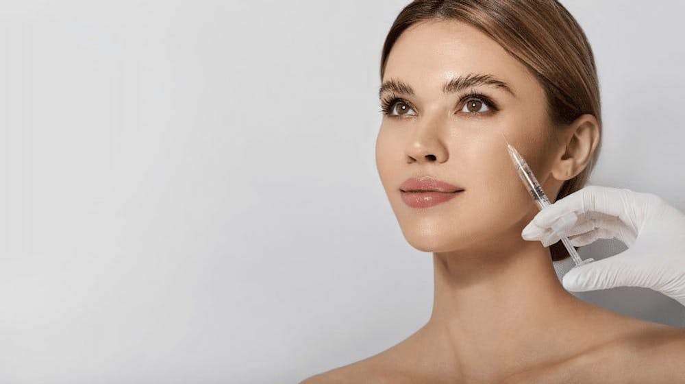 A woman receiving a hyaluronic acid injection on her cheek as part of a beauty treatment, performed by a professional.