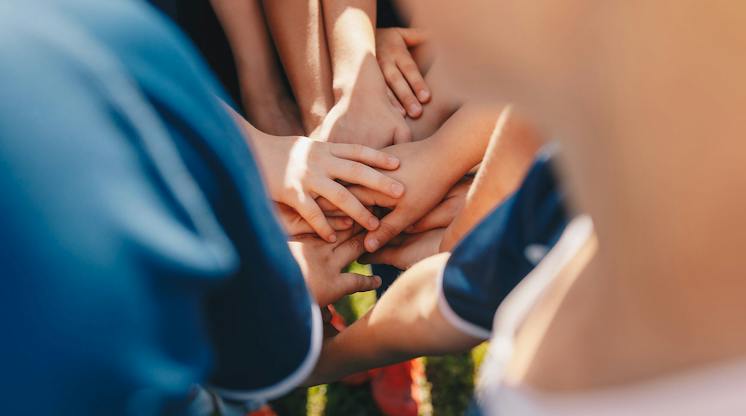 Close-up of youth sports teammates stacking their hands together in a huddle