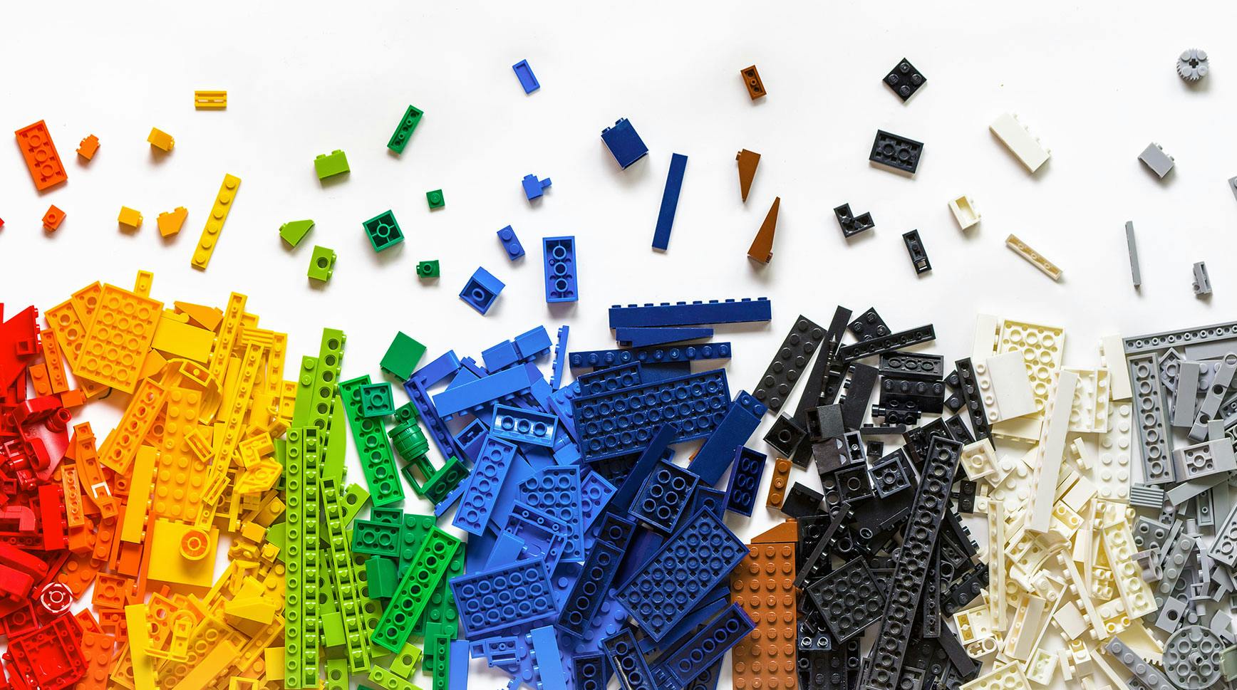 Loose Lego bricks sorted into a rainbow of piles on a white surface