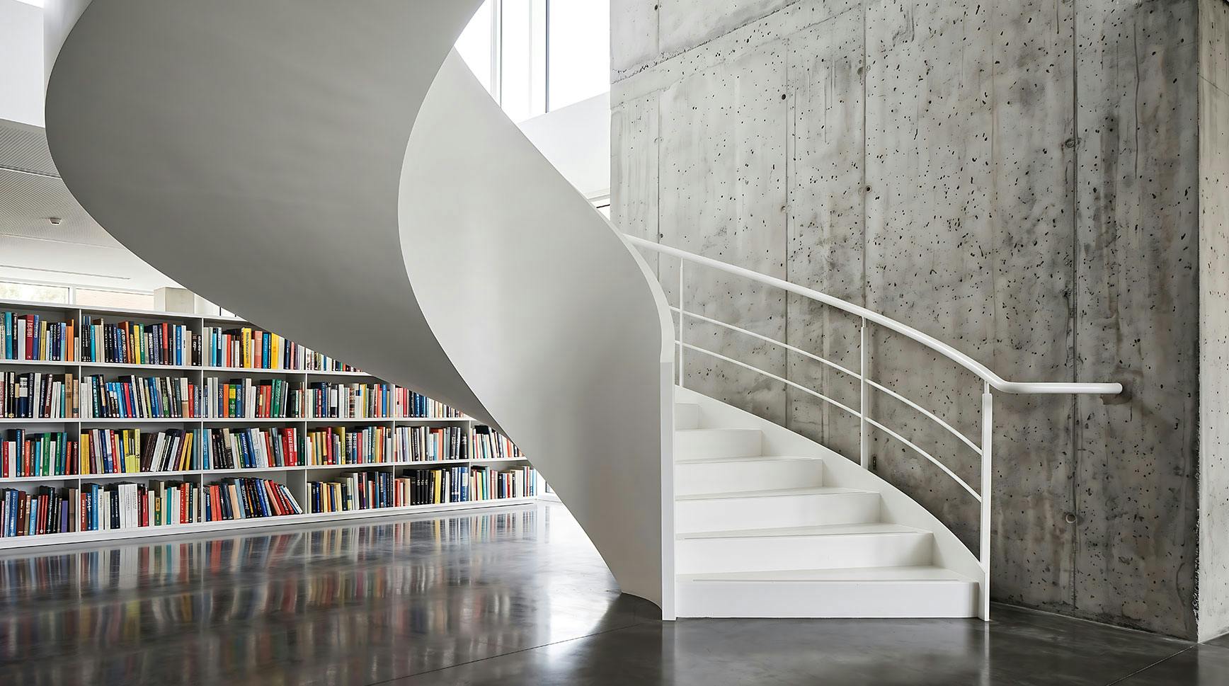 White spiral staircase in a modern library beside a wall of colorful bookshelves