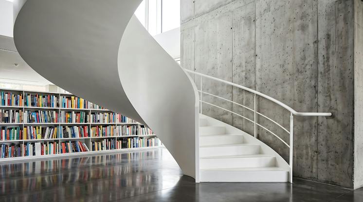 White spiral staircase in a modern library beside a wall of colorful bookshelves