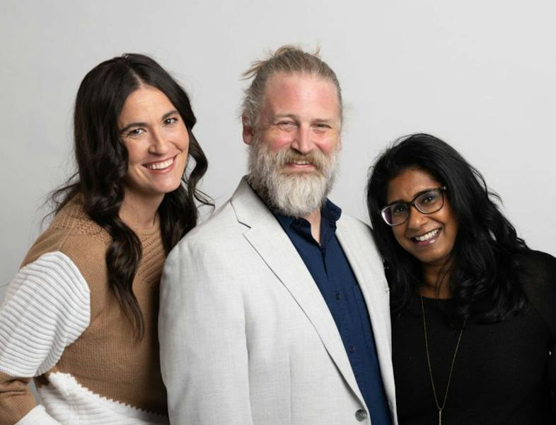 Three Ample team members smiling together against a light studio backdrop