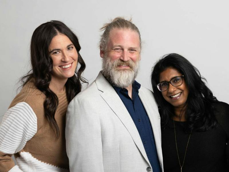 Three Ample team members smiling together against a light studio backdrop