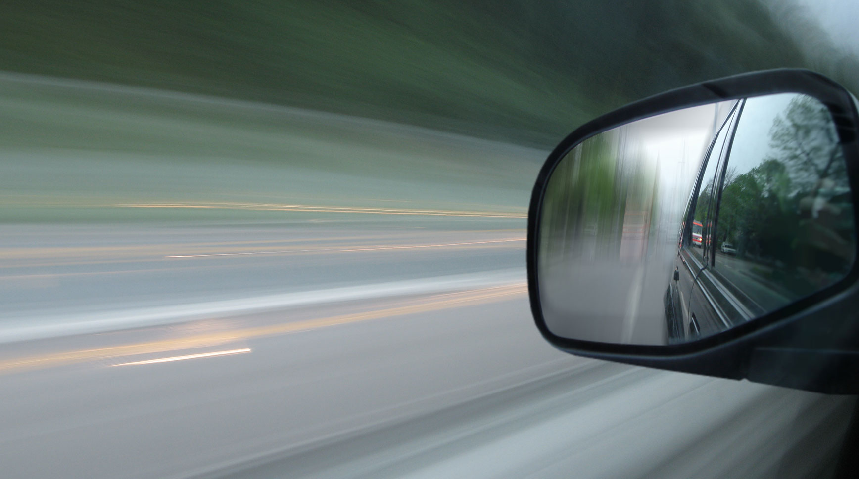 Motion-blurred view from a moving car with the road behind reflected in the side mirror