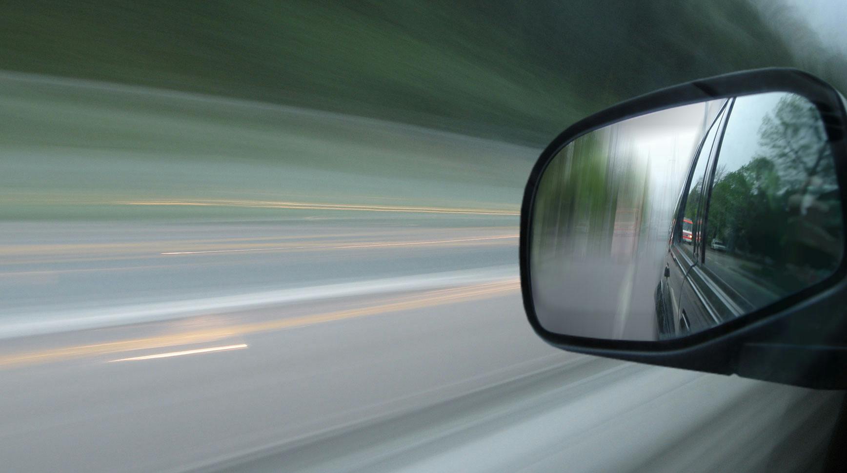 Motion-blurred view from a moving car with the road behind reflected in the side mirror