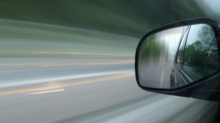 Motion-blurred view from a moving car with the road behind reflected in the side mirror