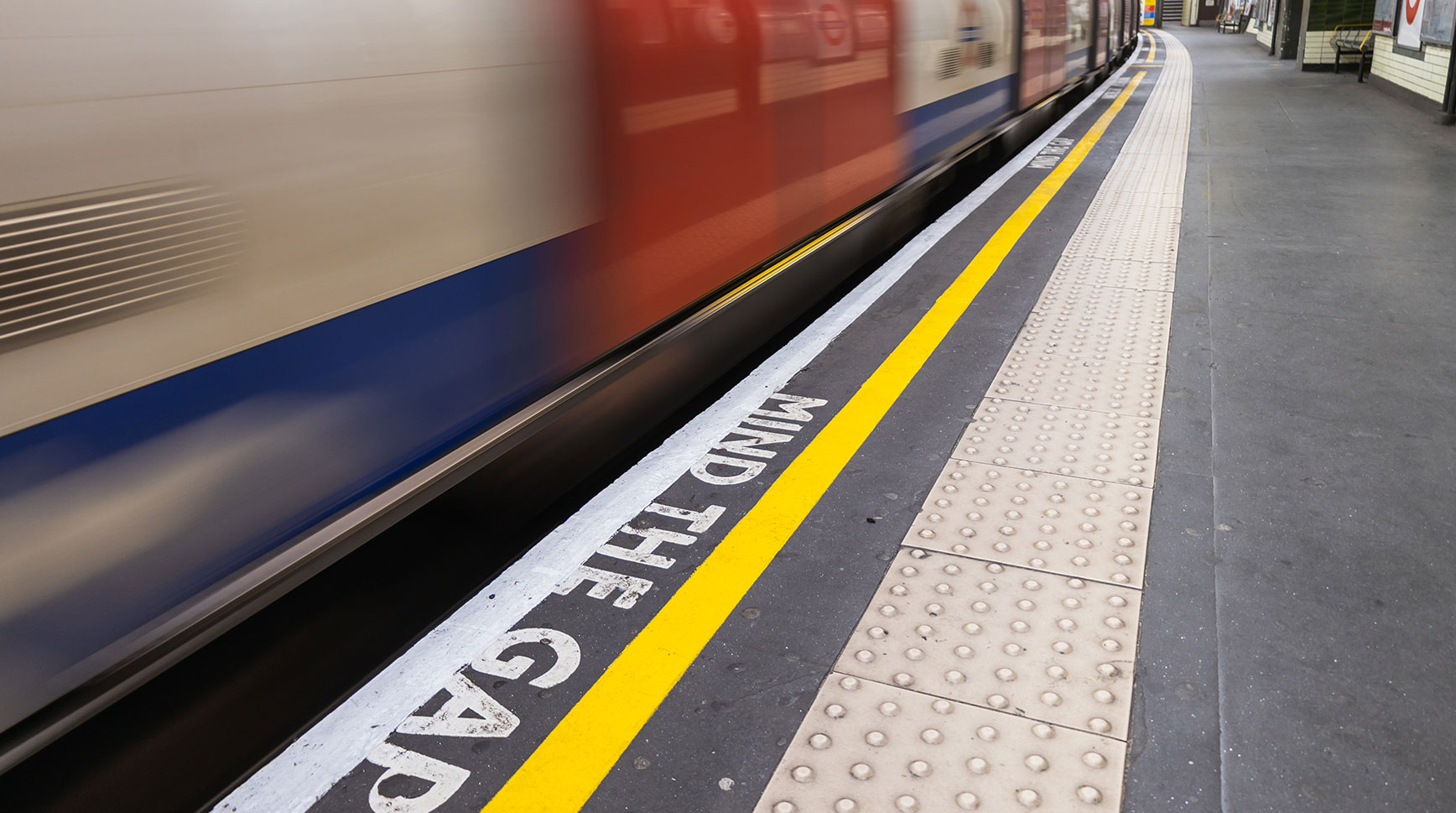 Blurred London Underground train passing a platform edge painted with the words Mind the Gap