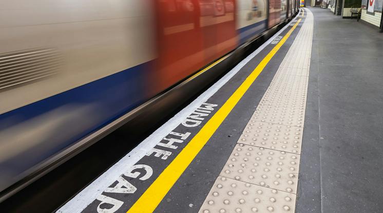 Blurred London Underground train passing a platform edge painted with the words Mind the Gap