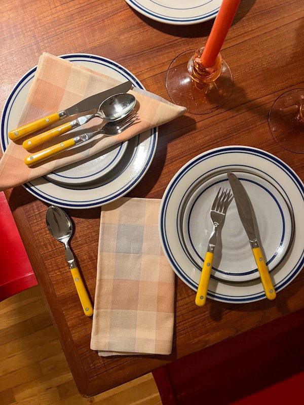 Dinner table setting with yellow flatware and striped napkins