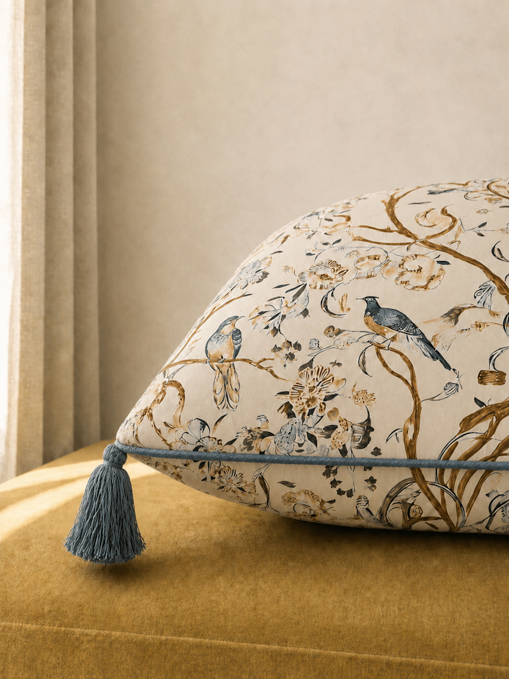 Throw pillow with a chinoiserie bird pattern on a mustard sofa