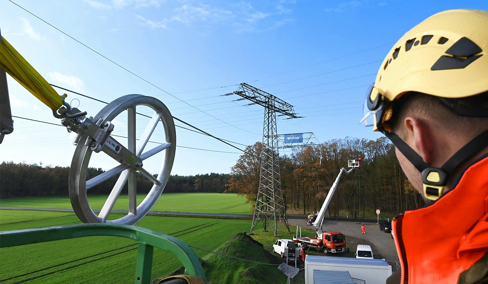WT Energiesysteme Mitarbeiter bei Arbeiten an einer Hochspannungsfreileitung mit Leiterseil und Seilrolle am Strommast.
