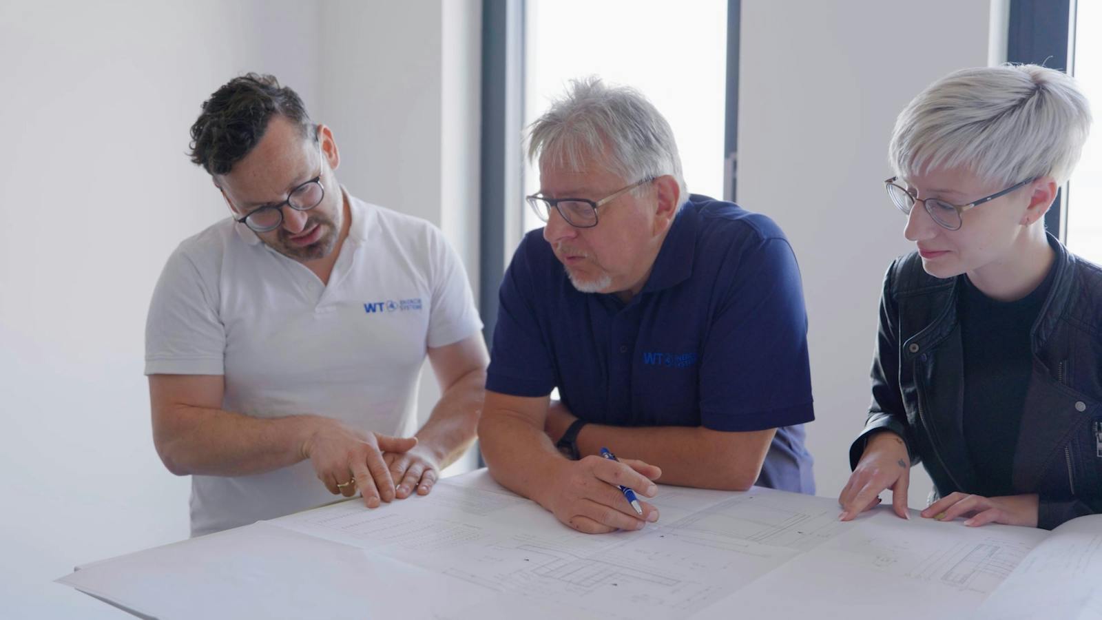 Drei Mitarbeitende von WT Energiesysteme besprechen gemeinsam technische Planungsunterlagen für Umspannwerke und Energieinfrastruktur.