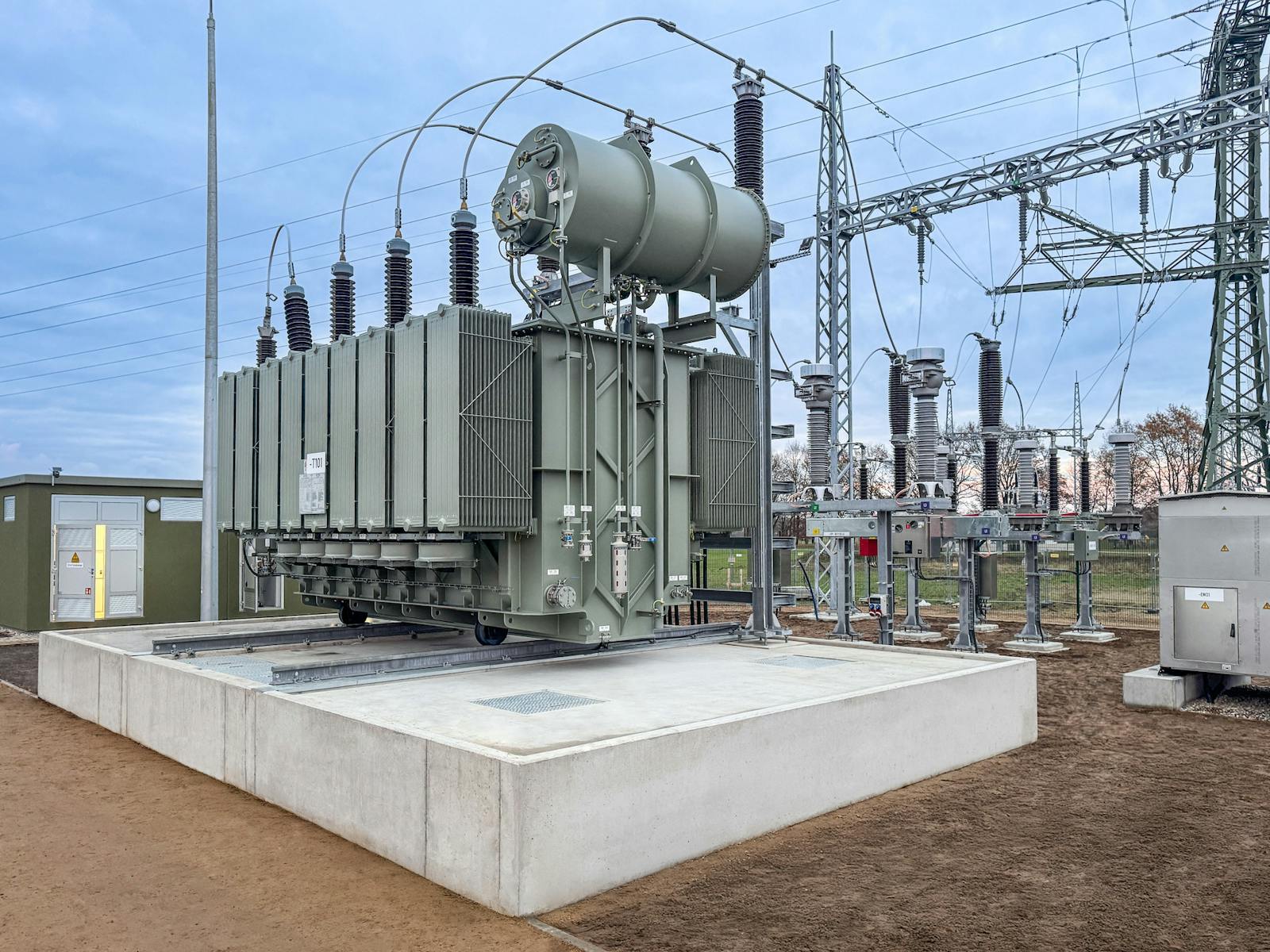 Leistungstransformator eines Umspannwerks auf einem Betonfundament mit Hochspannungsschaltanlagen, Isolatoren und Stahlkonstruktionen zur Anbindung an das Stromnetz.