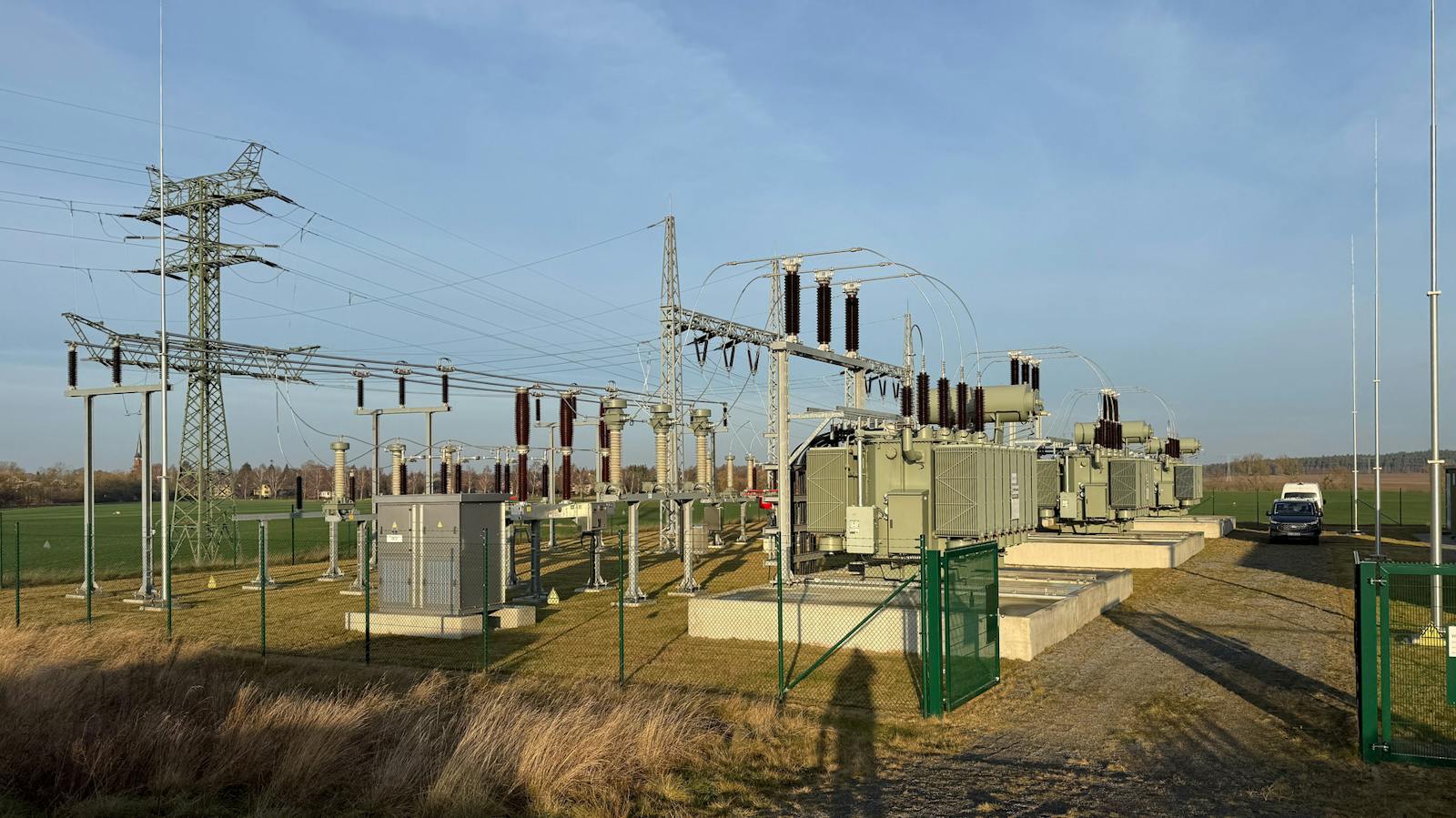 Umspannwerk mit mehreren Leistungstransformatoren, Hochspannungsschaltanlagen und Freileitungsanbindung über einen Stahlgittermast zur Einspeisung und Verteilung elektrischer Energie.