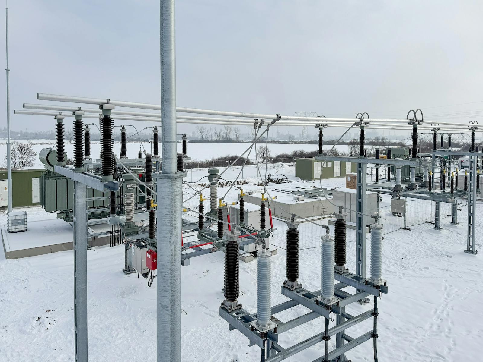 Verschneites Umspannwerk mit Leistungstransformatoren, Hochspannungsschaltanlagen, Isolatoren und Sammelschienen zur Übertragung und Verteilung elektrischer Energie.
