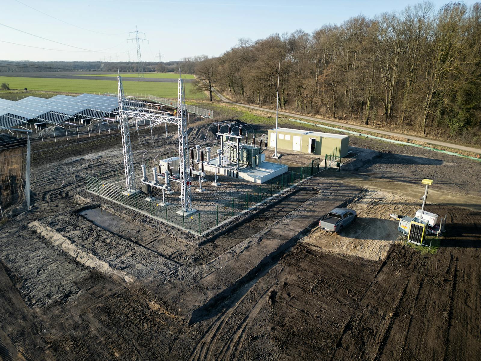 Luftaufnahme eines Umspannwerks mit Leistungstransformator, Hochspannungsschaltanlagen, Stahlgitterportal und Betriebsgebäude zur Netzanbindung einer angrenzenden Photovoltaikanlage.