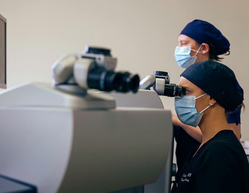 Two masked clinicians operating ophthalmic diagnostic equipment during an eye procedure