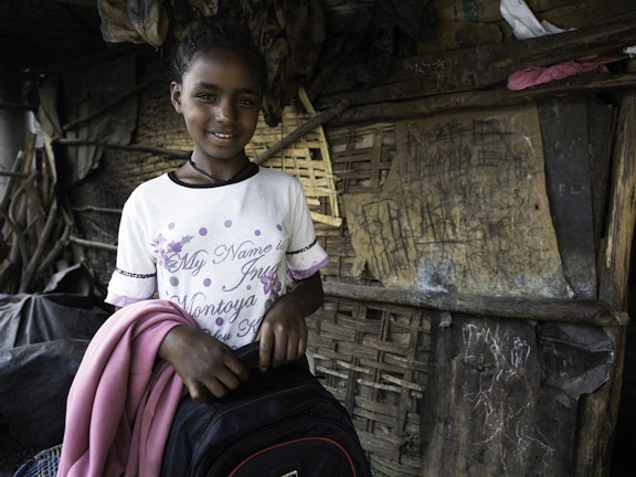 Young girl smiling to camera, holding her schoolbag
