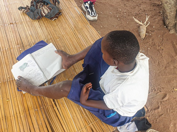 Magaiwa using her feet to read pages of a book, photo credit: ATFGM