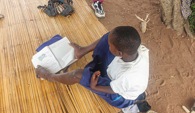 Magaiwa using her feet to read pages of a book, photo credit: ATFGM