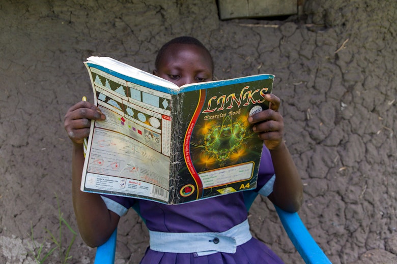Faith reading a book while seated outside their house.