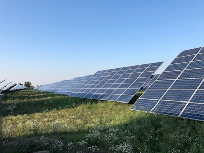Rows of ground-mounted solar panels in a green field in Piedmont, Italy.