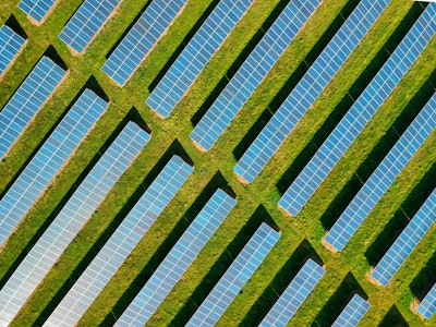 An aerial view of rows of solar panels arranged on a green field.