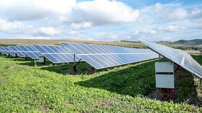 Blue solar panels on green grass field under white clouds and blue sky during daytime.