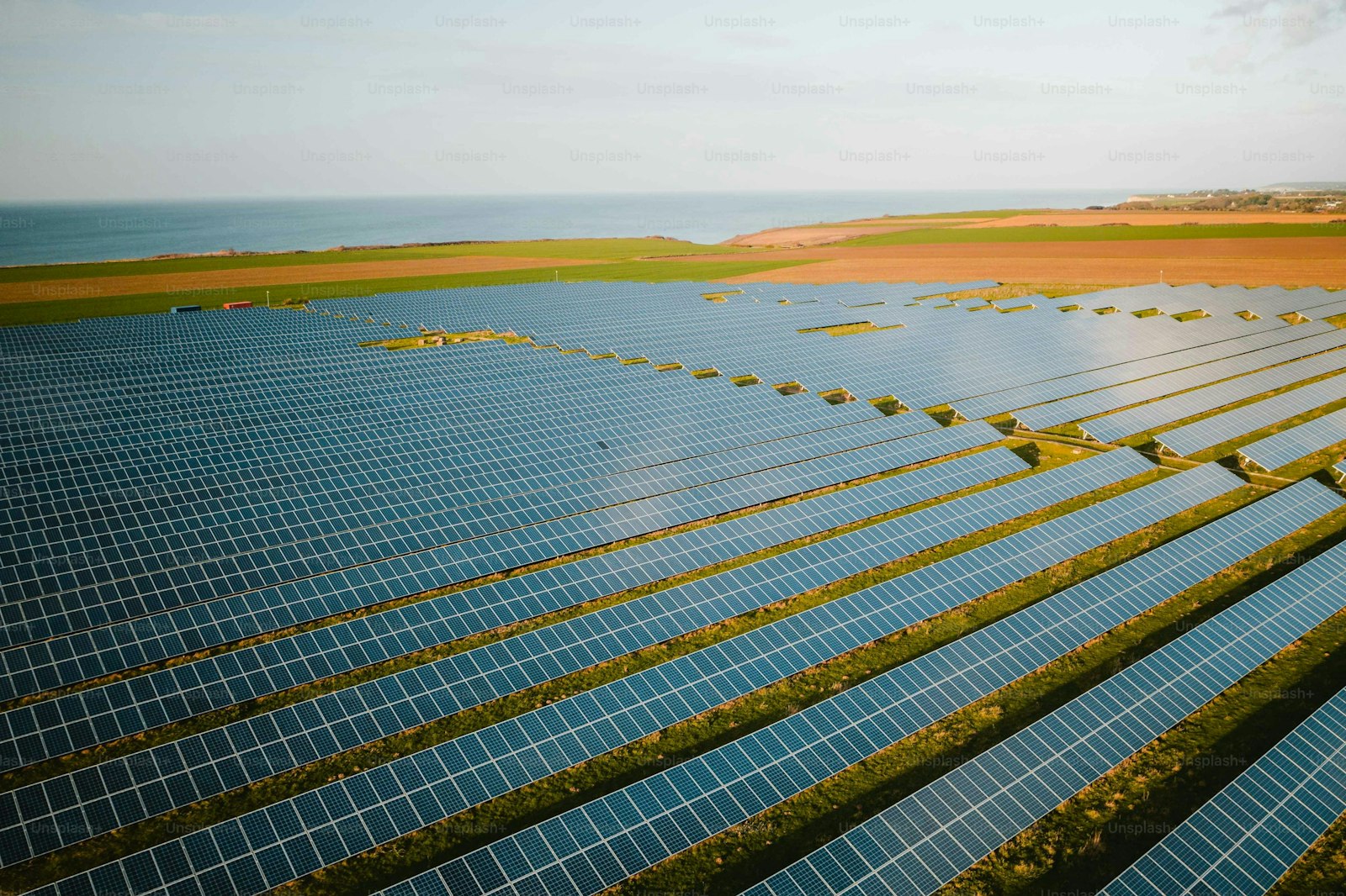 Rows of solar panels in a field near the ocean.