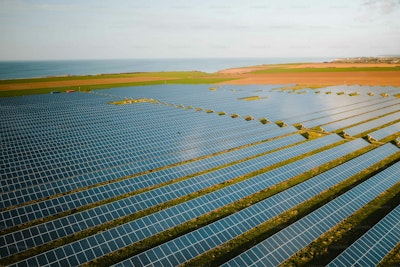 Rows of solar panels in a field near the ocean.
