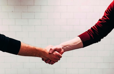Two person shaking hands near white painted wall.
