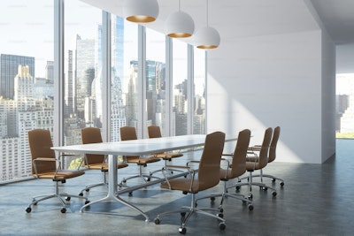 A modern conference room with a white table and brown chairs overlooking a city.