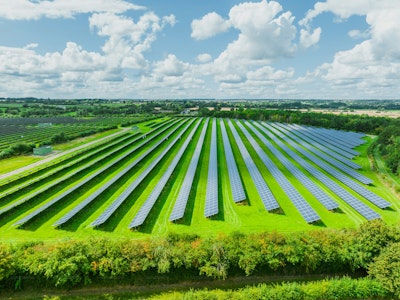 Aerial view of solar panels on green field at suburb in sunny day.