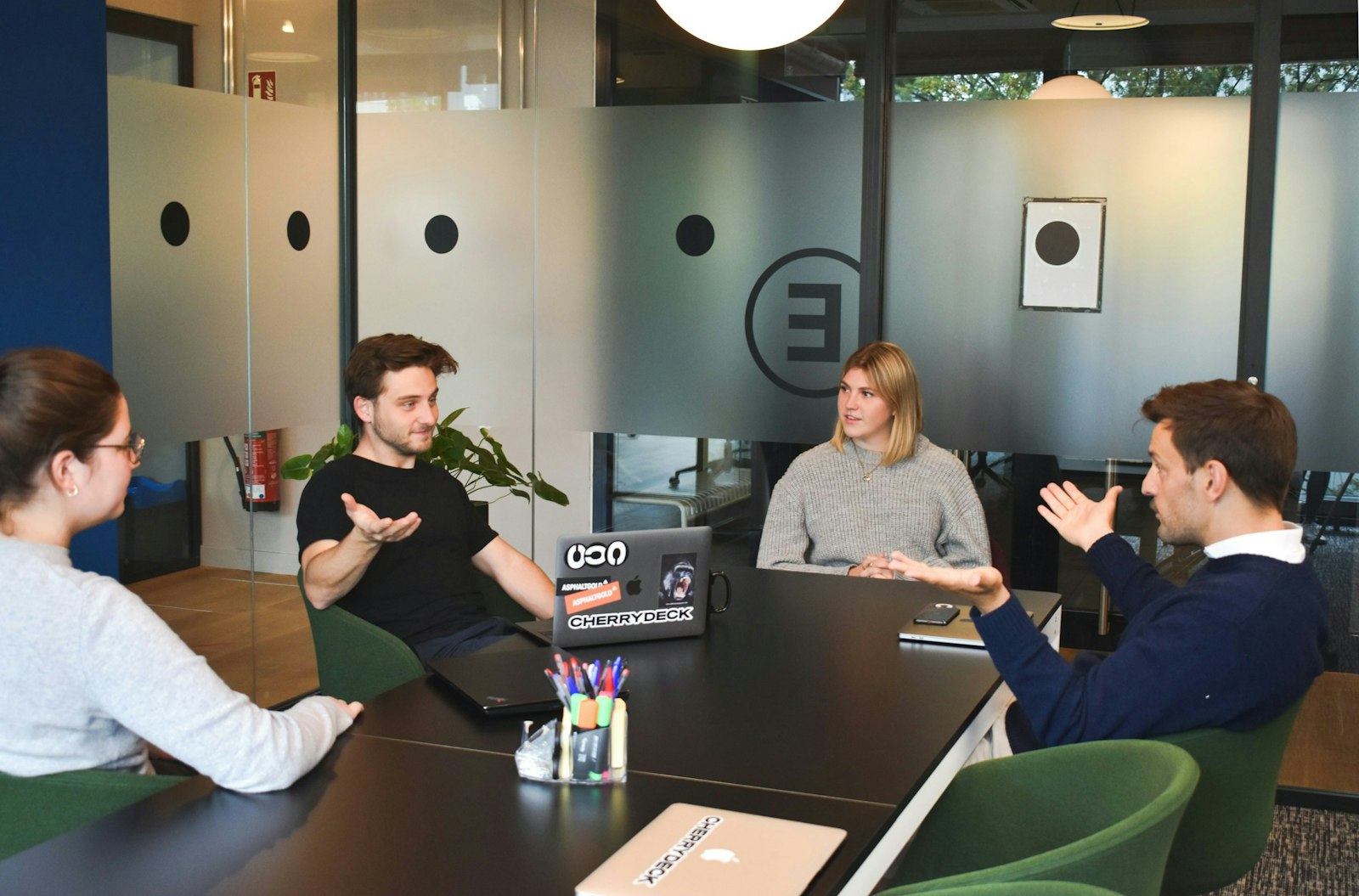 Four people in a meeting around a black table in a modern office.