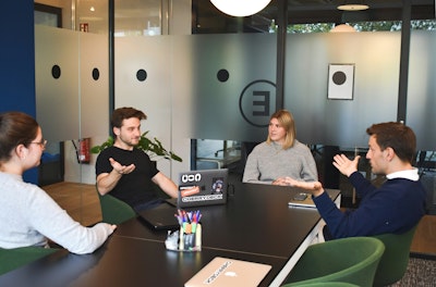 Four people in a meeting around a black table in a modern office.