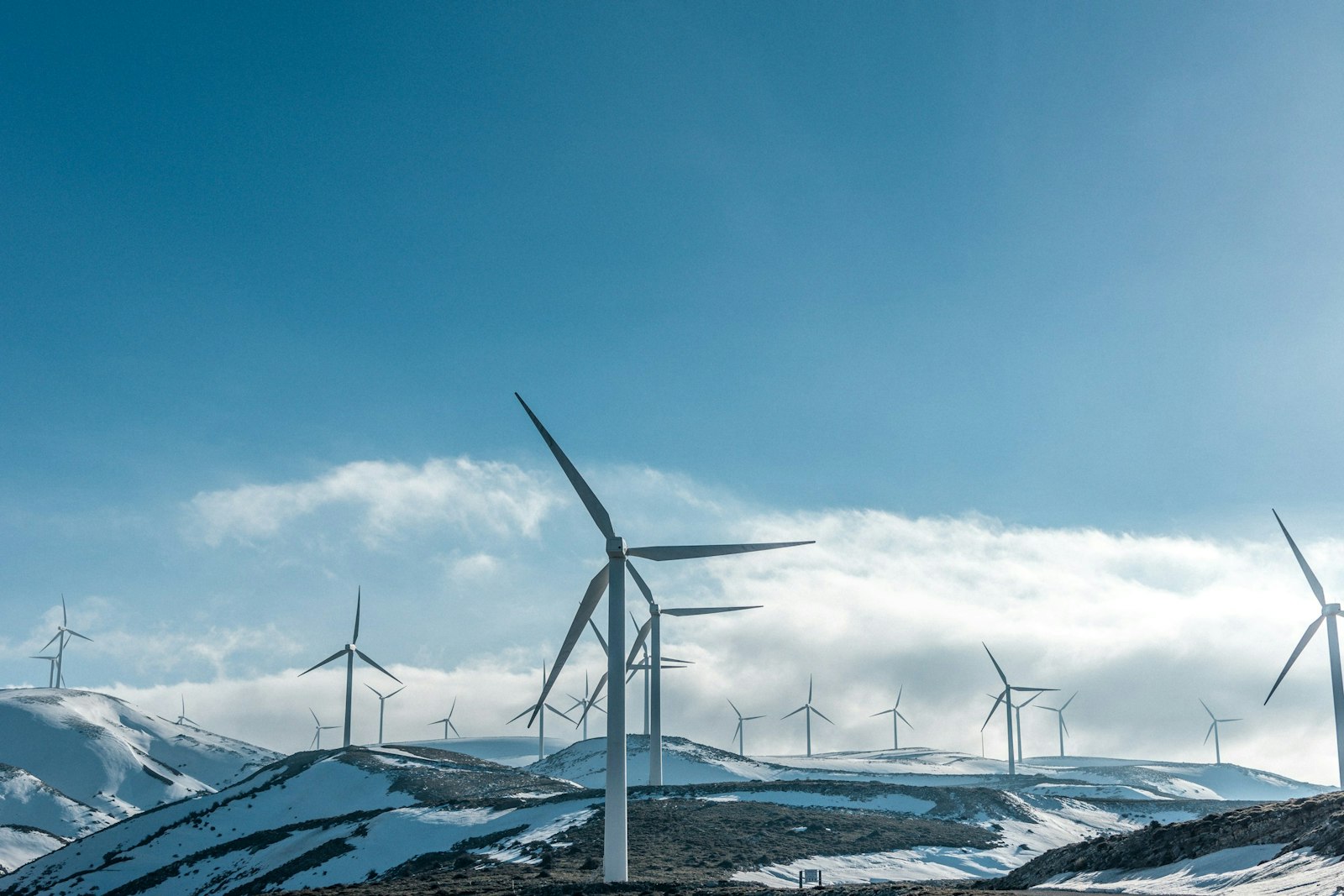 Wind turbines on snowy mountain under clear blue sky during daytime.