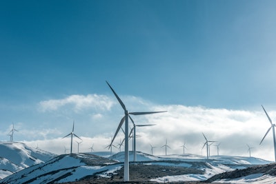 Wind turbines on snowy mountain under clear blue sky during daytime.